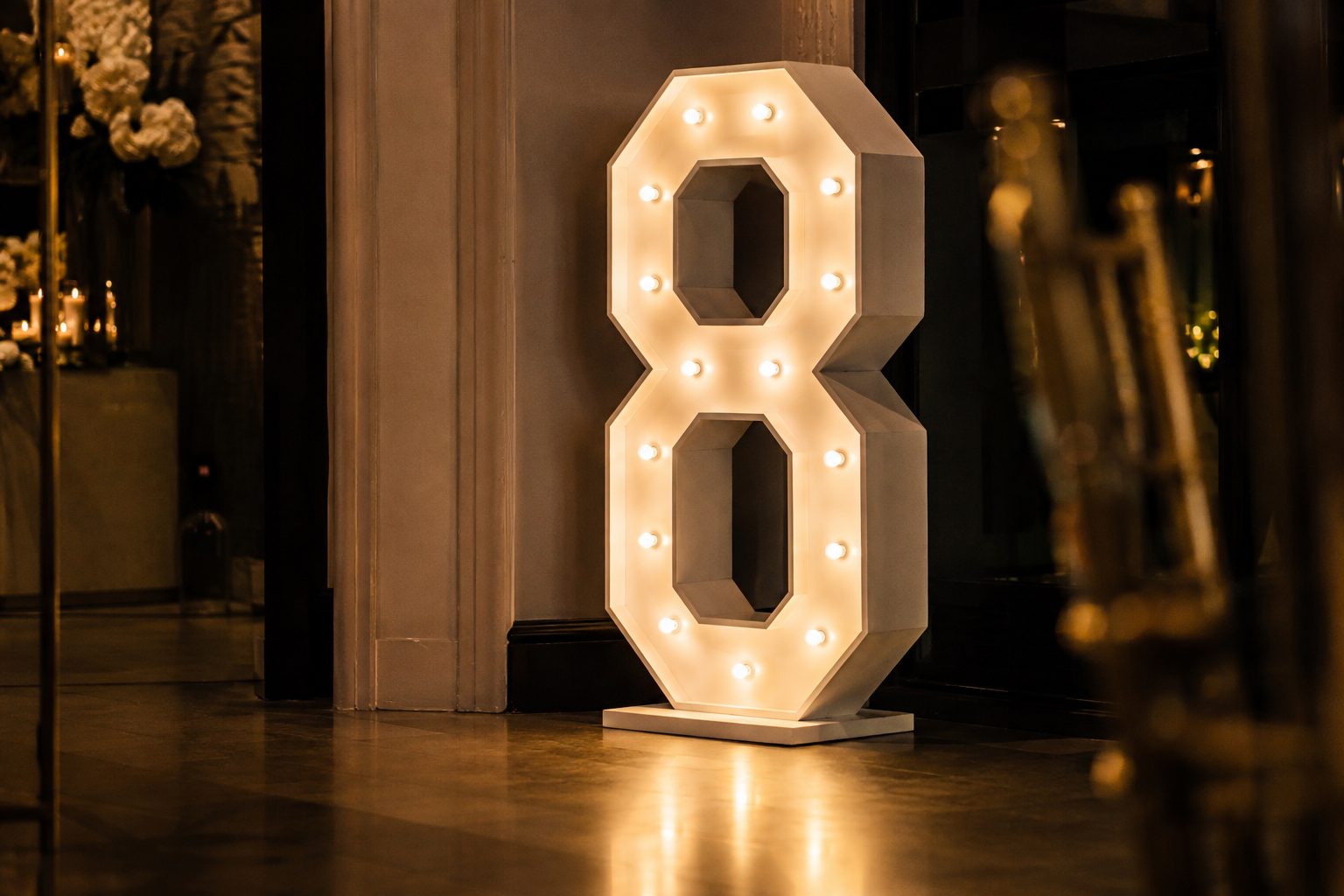Large illuminated light-up number glowing warm-white inside an elegant event venue